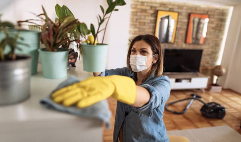 Woman in shirt and yellow gloves wearing mask scrubbing with cloth inside a room