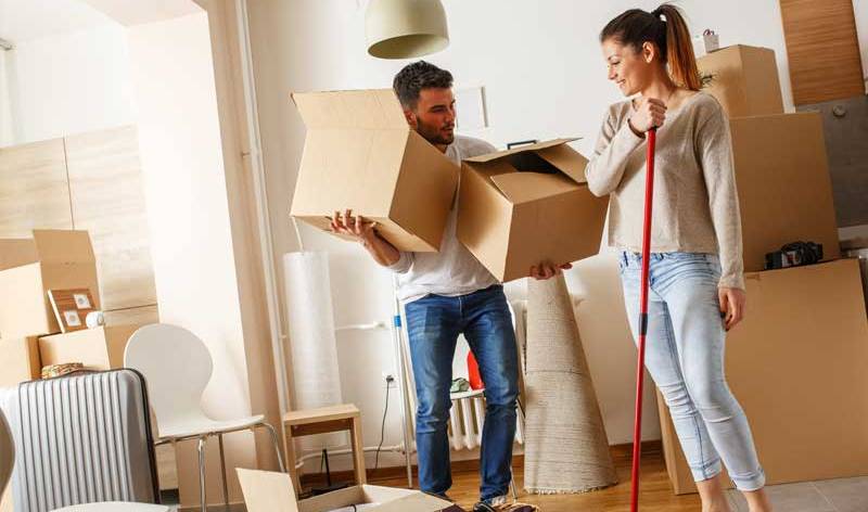 A man holding two boxes and a woman holding wiper in hand inside a room