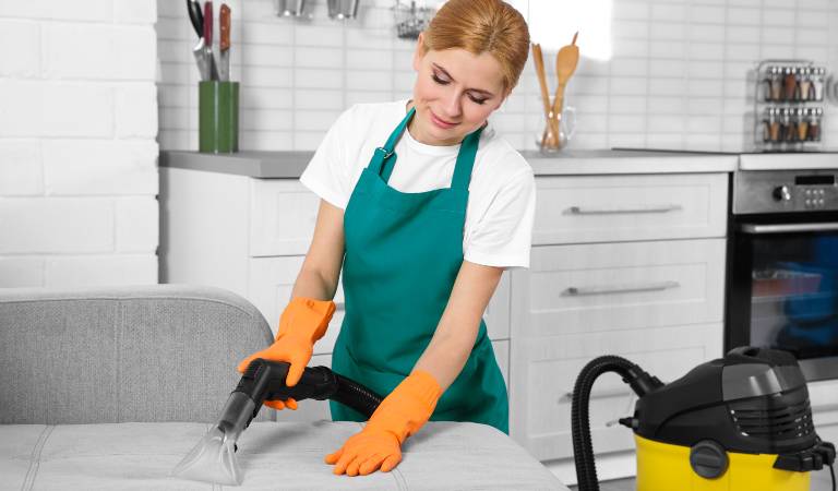 Woman in white green dress vacuuming sofa inside a living room