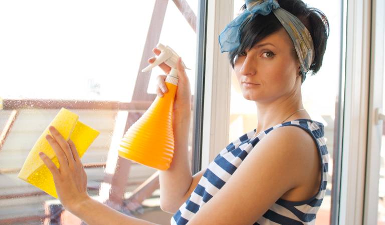 Woman in white-blue sleeveless top holding a yellow bottle in one hand and a yellow cloth in second hand