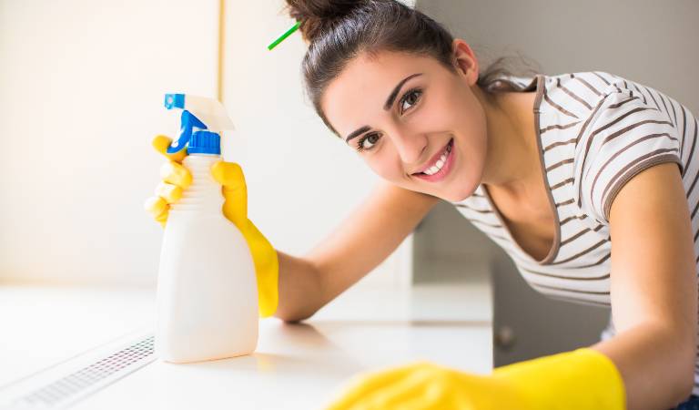 Woman in white top and yellow gloves holding a white bottle with blue cap