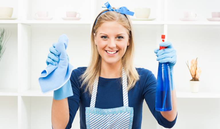 Woman in blue dress holding a blue bottle in one hand and cloth in her second hand