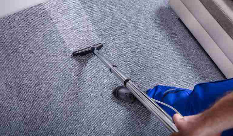 Man in blue uniform vacuuming carpet with a vacuum cleaner
