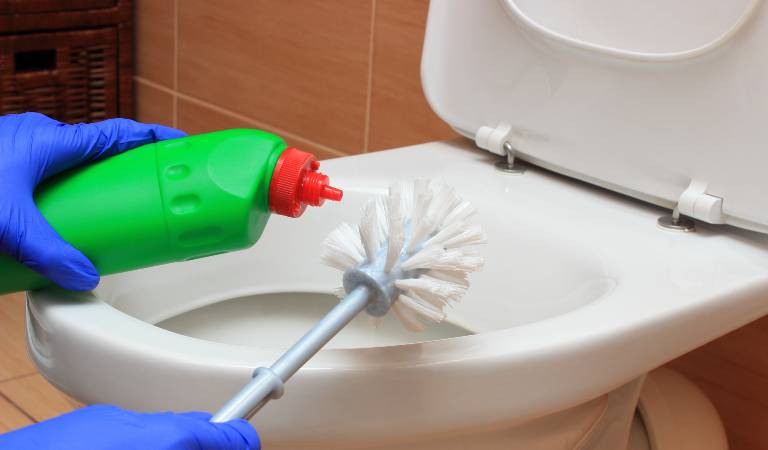 Hand of woman in blue glove cleaning toilet bowl using brush.