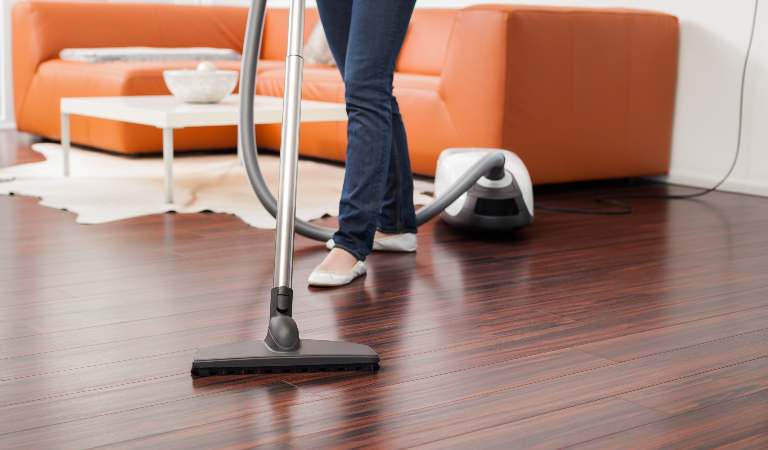 Woman is using vacuum cleaner on wooden floor.