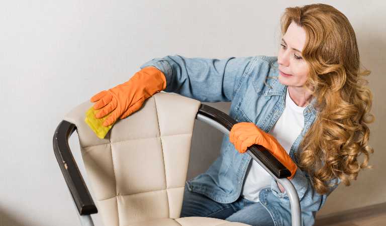 Woman in orange glove cleaning leather furniture with a yellow cloth.