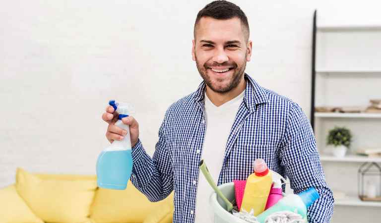 A man in check shirt holding a bottle in one hand and a basket filled with tools in second hand.