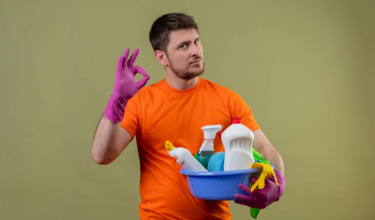 Man in orange t-shirt holding a cleaning basket filled with tools, bottles.