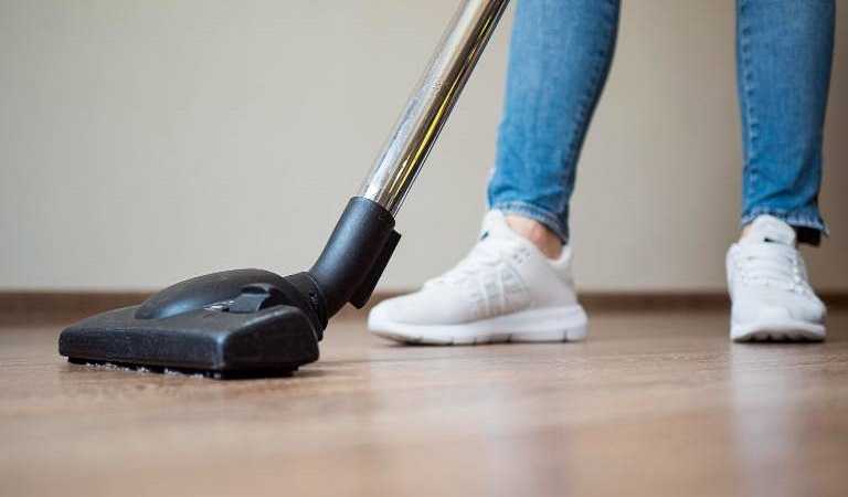 Woman in blue jeans and white shoes vacuuming floor with vacuum cleaner.