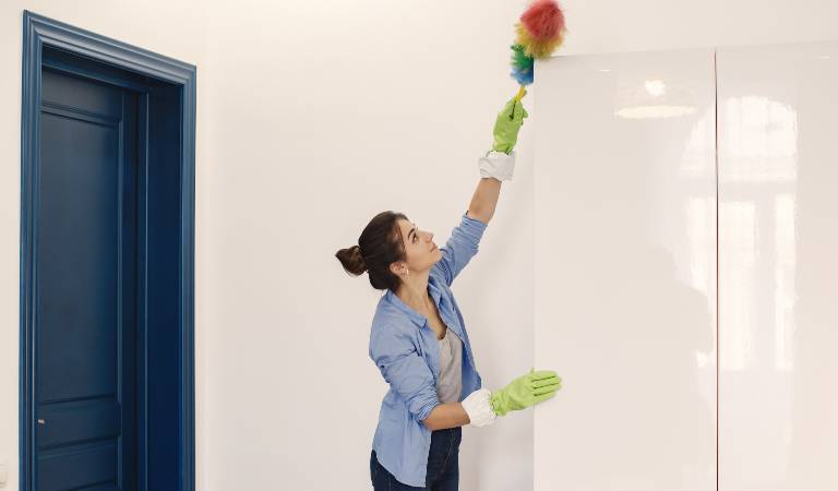 Woman in shirt and green glove cleaning almira with a stick.