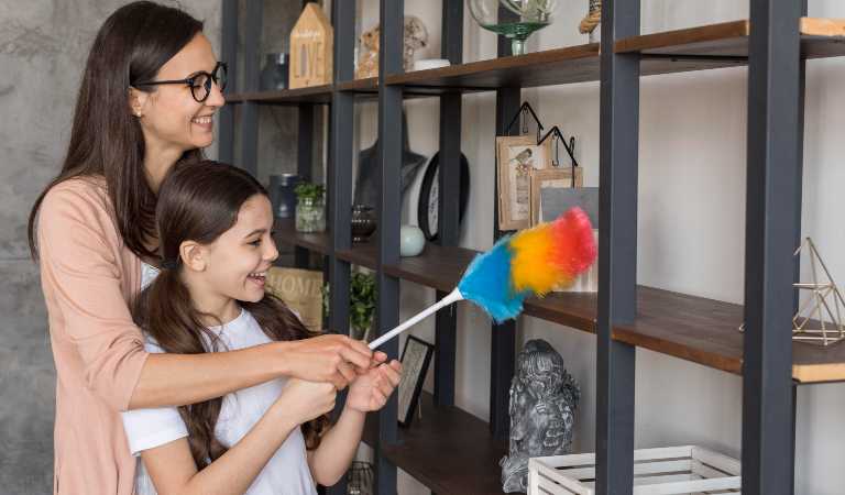 Smiling woman with her daughter dusting inside her house