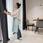 Woman holding her curtain inside her living room.