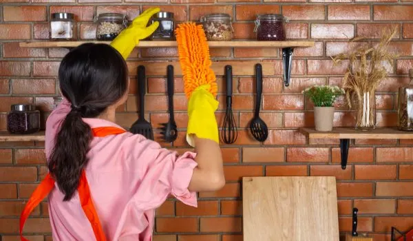 girl is wearing yellow gloves while cleaning the kichen room with duster in house