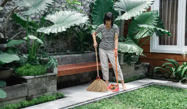 Housewife cleaning yard with sweeping leaves on the backyard sidewalk