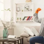 Spring-cleaning done. Happy man with raised hands standing on one knee in clean appartment among detergents, bucket and dusters