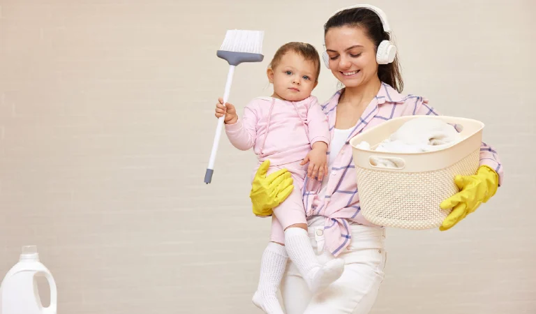 Happy mother housewife is holding cute baby girl with broom in hand and basket in her hand