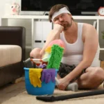 Pensive man sitting on floor near vacuum cleaner and bucket