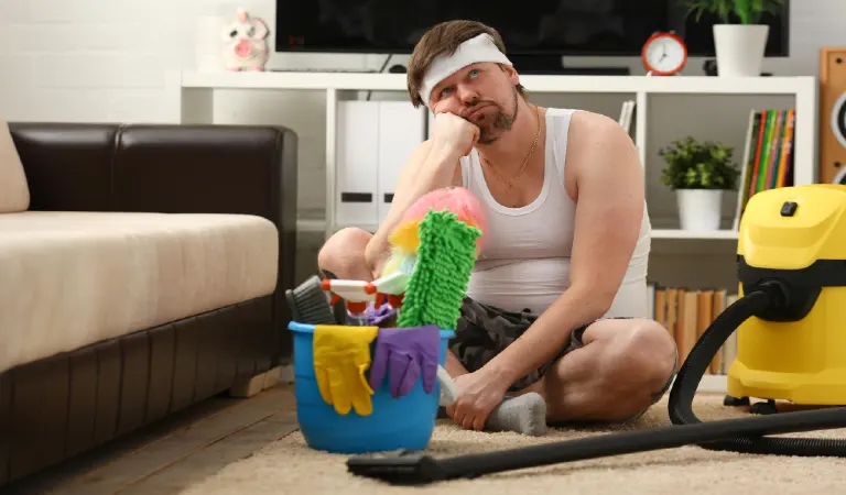Pensive man sitting on floor near vacuum cleaner and bucket