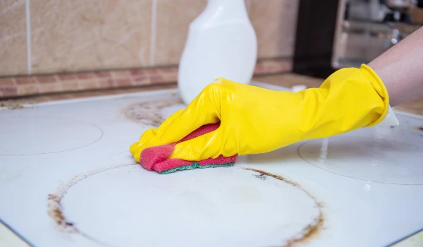 Cleaning stainy stove with sponge and gloves