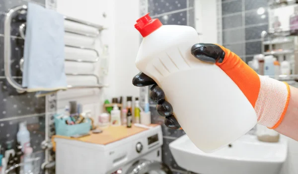 Man's hand in protective glove with bottle of washing liquid in bathroom