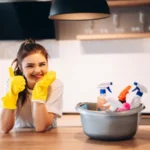 Young happy woman in yellow gloves is cleaning her kitchen at home with detergents