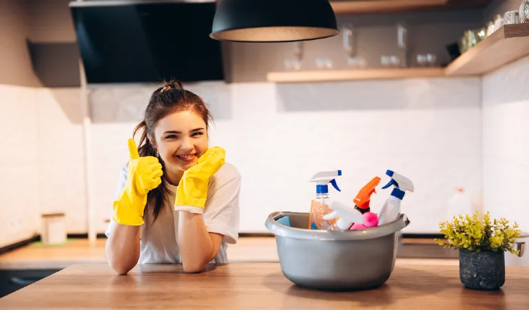 Young happy woman in yellow gloves is cleaning her kitchen at home with detergents